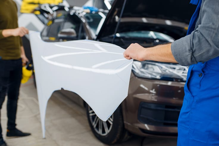 Professional installer holding a transparent film template designed to protect a car's paint from scratches and chips.