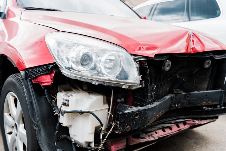 A close-up of a red car's damaged bumper and fender after a collision.