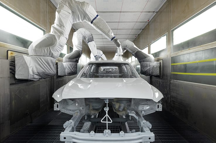 A modern automotive production line where car bodies are being painted by automated robots in a clean and efficient environment.