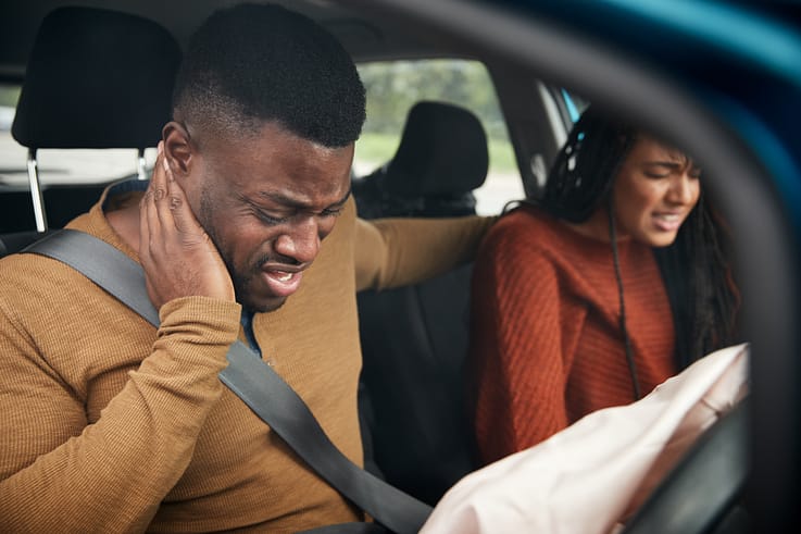 A woman comforts a man experiencing whiplash pain after their car accident.