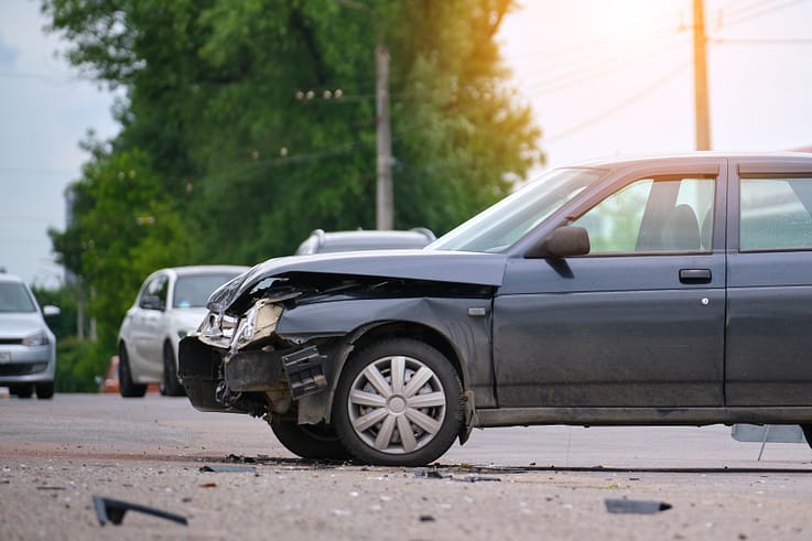 Aftermath of a car crash on a busy city street, showing a wrecked vehicle with deployed airbags and debris scattered around.