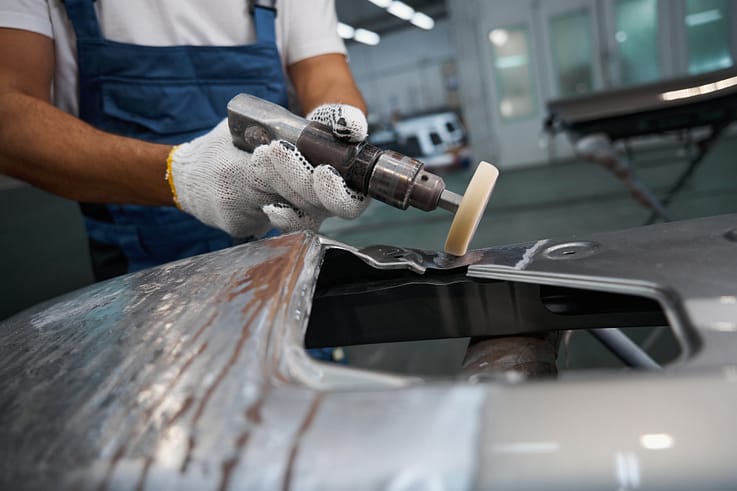 Auto body specialist removing imperfections from a car's paint using a polishing machine.