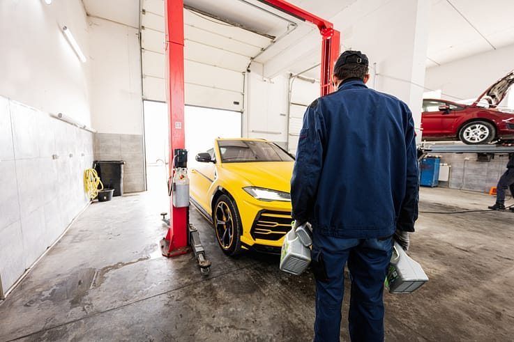 Automotive technician preparing for an oil change on a yellow SUV, holding various oil containers.