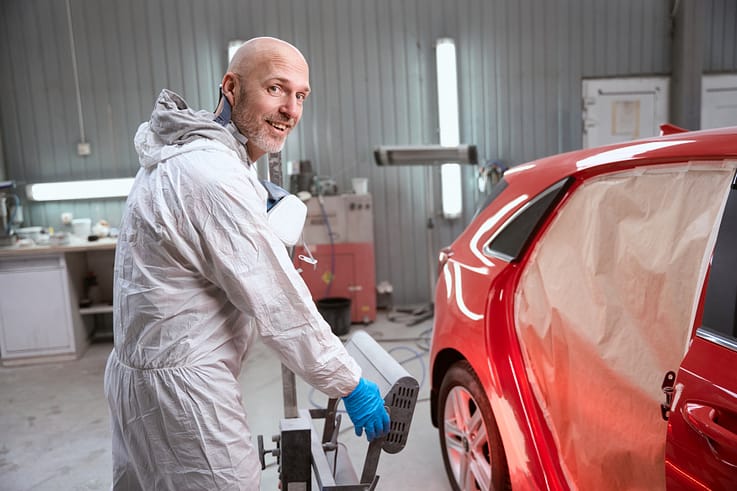 Skilled worker employing an infrared lamp to ensure a smooth and durable finish on a primed car surface.