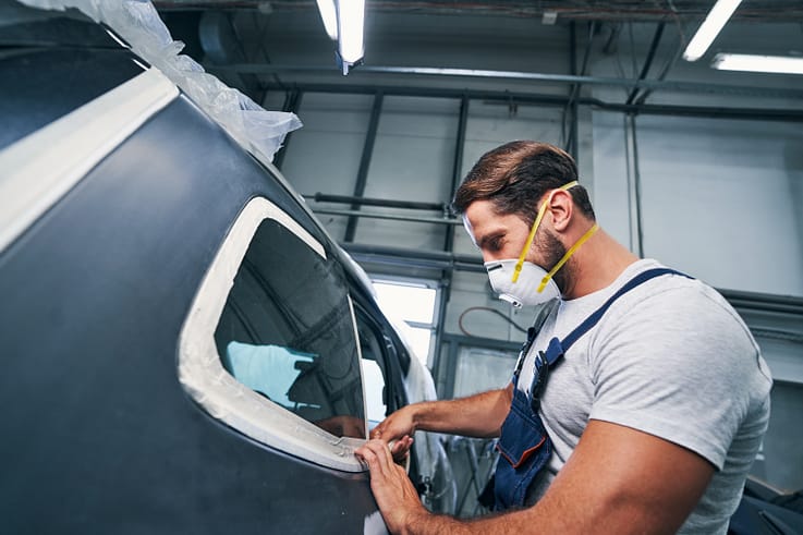 A worker using duct tape to temporarily seal a broken car window.