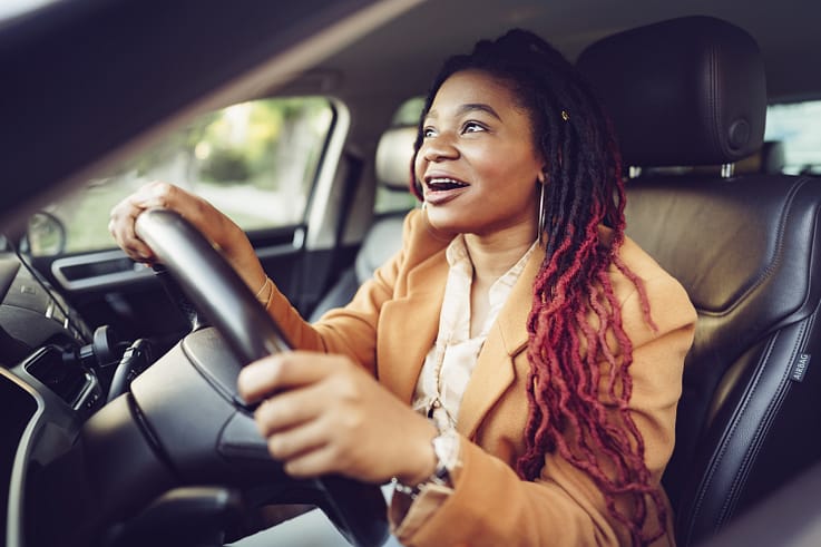 A smiling African American woman sitting in the driver's seat of a car.