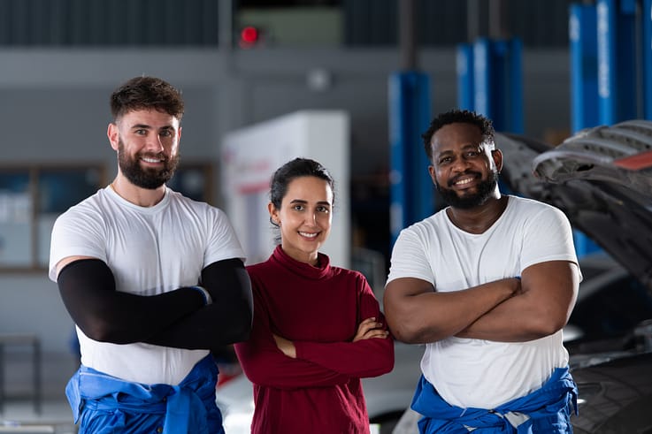 Diverse team of auto mechanics, two male and one female, posing for a portrait in their work uniforms.