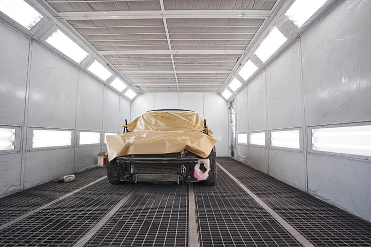 Car undergoing the painting process in a controlled environment, with a worker using a spray gun for a flawless finish.