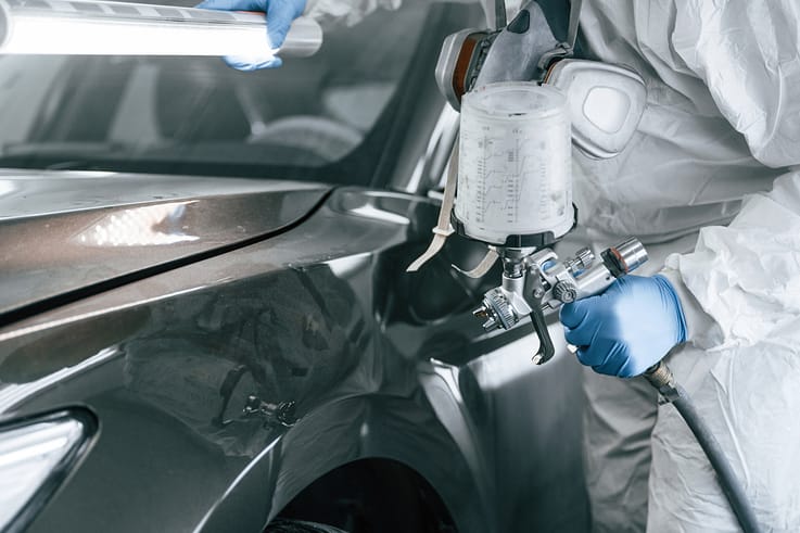 Worker in a cleanroom environment using a spray gun to achieve a flawless paint finish on a car.