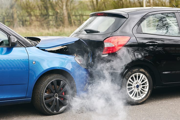 Aftermath of a devastating car crash showing two wrecked cars engulfed in smoke.