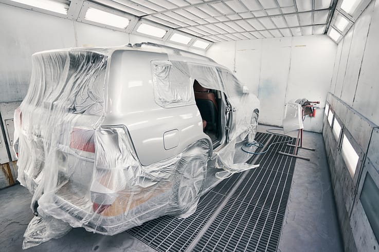 White van masked with protective film in a professional spray booth, ready for painting.