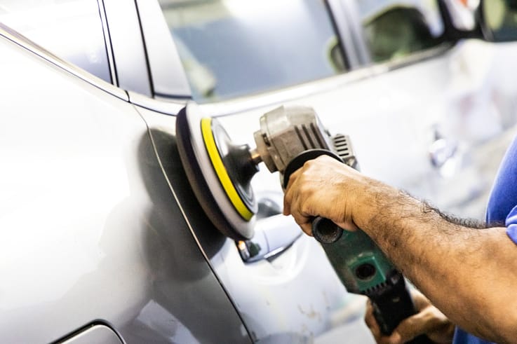 A worker is polishing a car with a grinder machine.