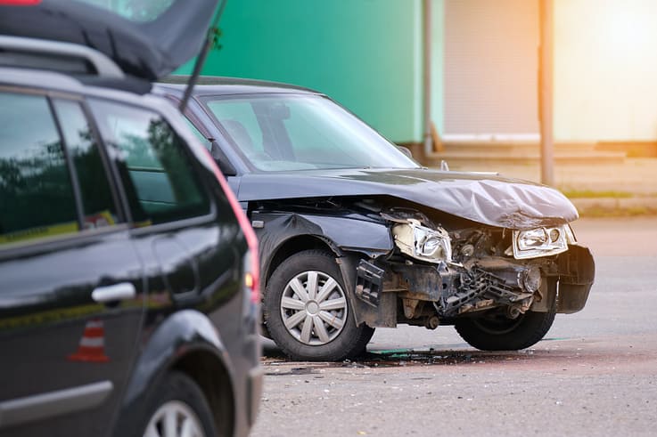 A damaged vehicle rests on a city street after a car accident, surrounded by debris.