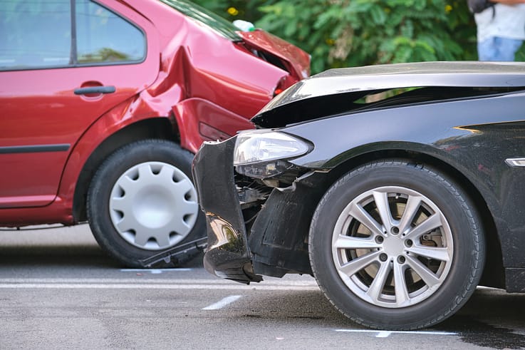 A photo of the aftermath of a car accident on a city street, showing two heavily damaged vehicles and debris scattered around.