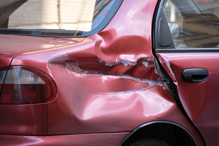 A dented silver car with a missing side mirror and scraped paint parked on the side of a city street in Atlanta.