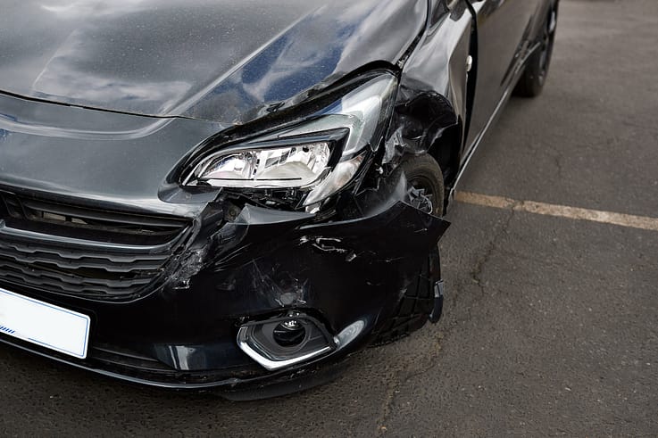 Close-up of a cracked and shattered headlight on a red car parked in a parking lot.