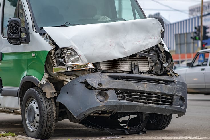 A heavily damaged car with crumpled metal and shattered glass after a collision on a city street.