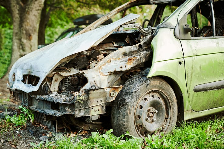 A close-up view of a burned car, with melted metal and shattered glass.