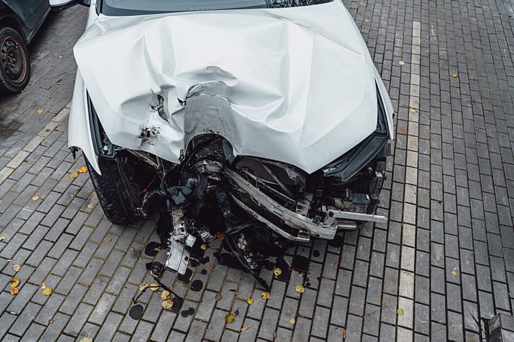 A totaled white car with a crushed front end and deployed airbags rests against a lamppost in Atlanta.