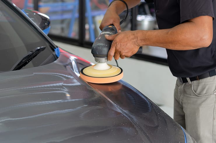 A professional auto detailer equipped with a polishing machine, preparing to remove swirls and scratches from a car's paintwork.